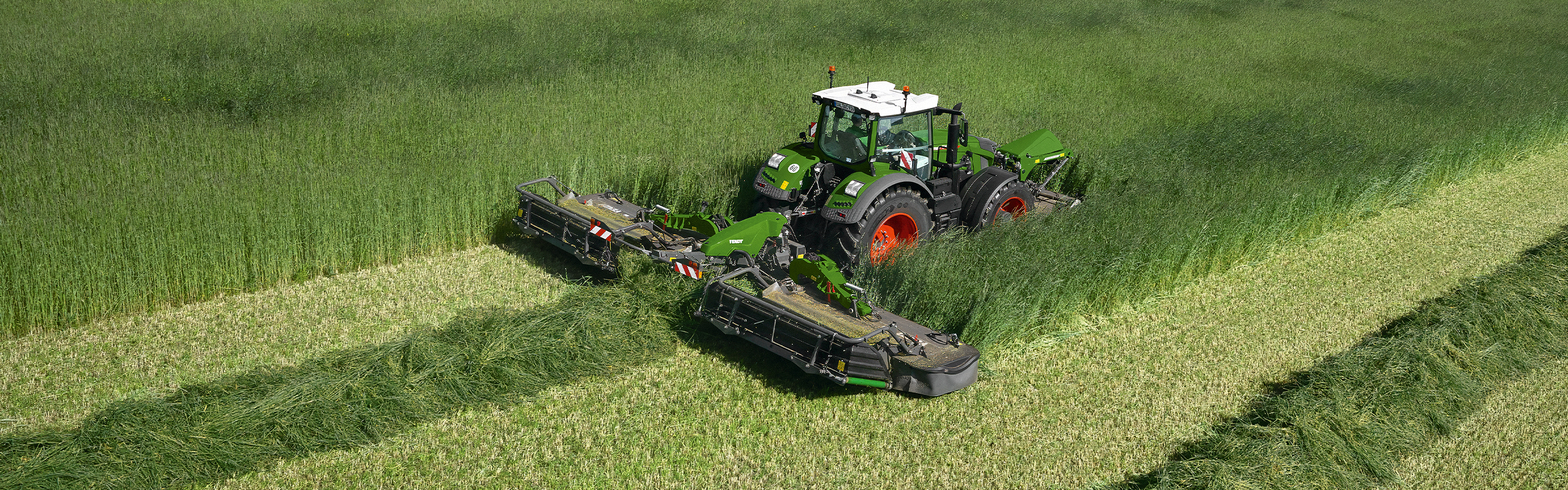 A farmer mows a green meadow with a Fendt Slicer front and rear mower.