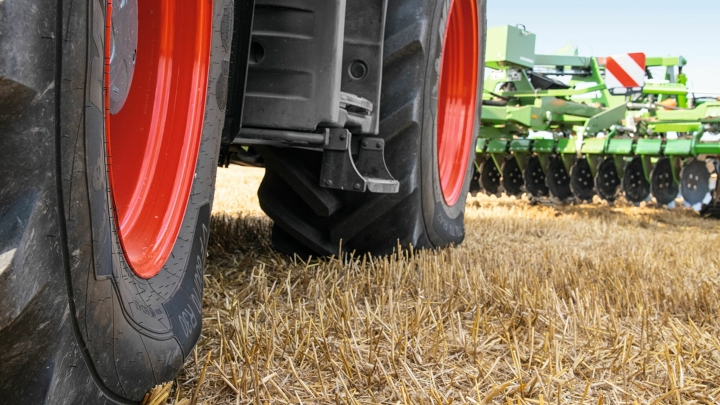 Close-up of a harvested grain field and a Fendt 700 Vario driving on it while protecting the soil