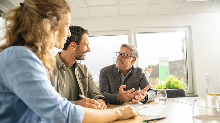 A farmer and farmer sit at a table with a Fendt dealer and get advice.