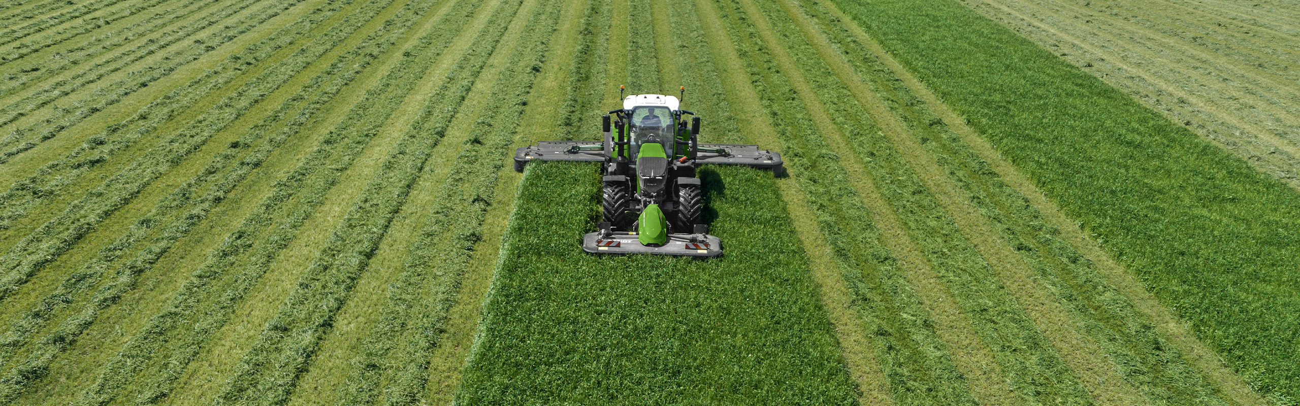 A farmer mowing a green meadow with a Fendt Slicer front and rear mower.