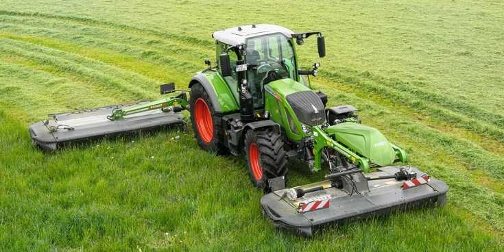 A farmer drives a Fendt Slicer fornt and rear mower in a meadow.