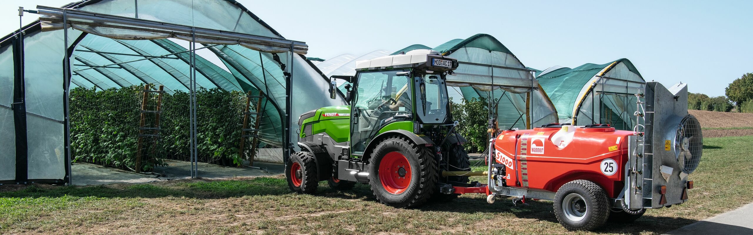 A green Fendt e100 V Vario driving into a greenhouse