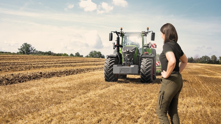 A farmer stands proudly in front of her Fendt 700 Vario Gen7 tractor on a stubble field.
