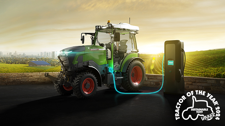 Fendt e107 tractor connected to a charging station in a field at sunrise, with the TOTY logo and the text “Tractor of the Year 2024 Sustainable TOTY”