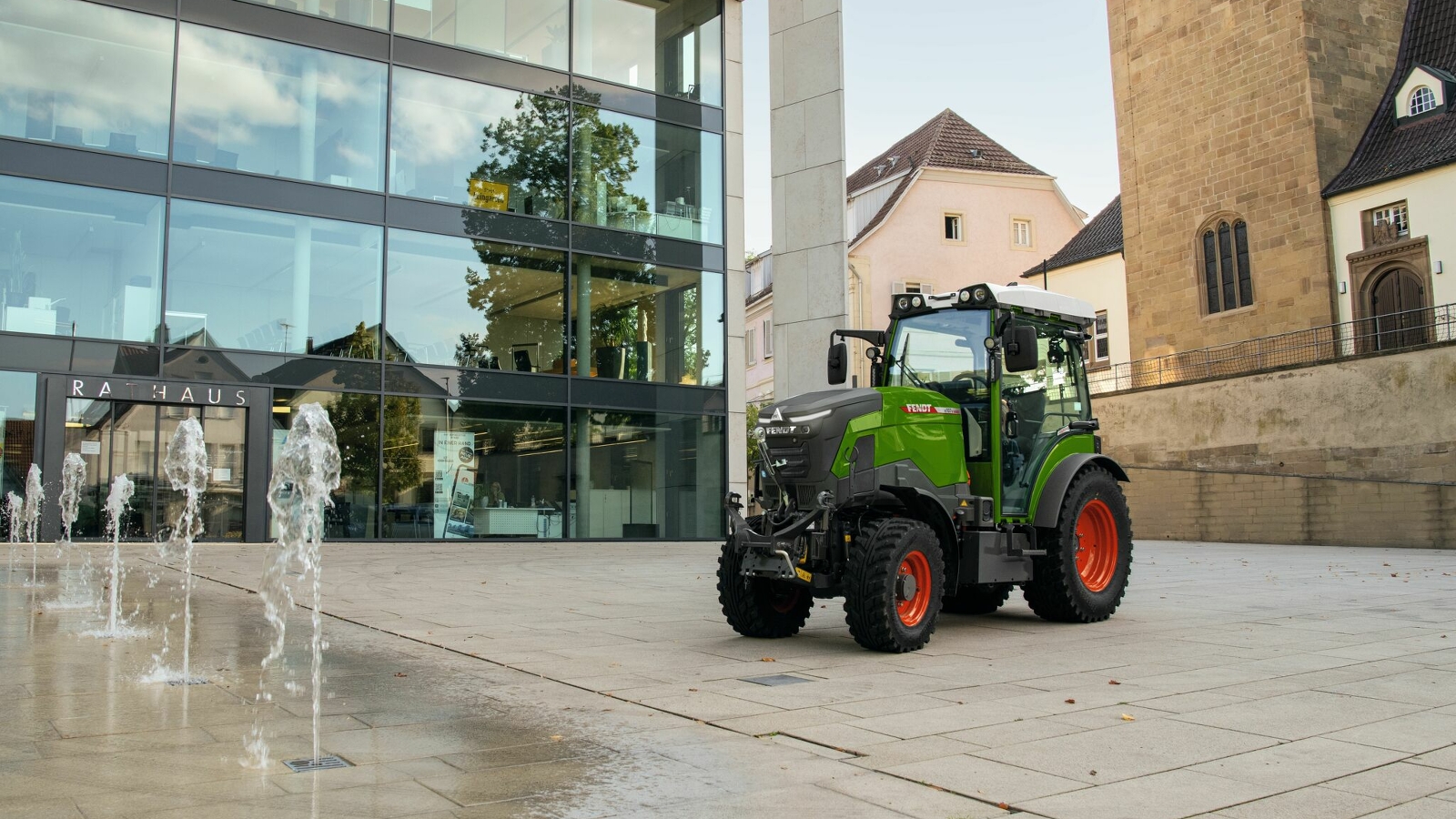 A green Fendt e100 V Vario with red rims standing in front of a building in the city