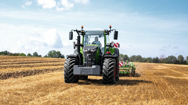 The Fendt 700 Vario Gen 7 in use in a field. In the background are trees and a blue sky with white clouds.