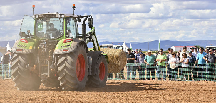 A Fendt tractor doing loading work with atraw bale, ppeople waching from behind a green fence