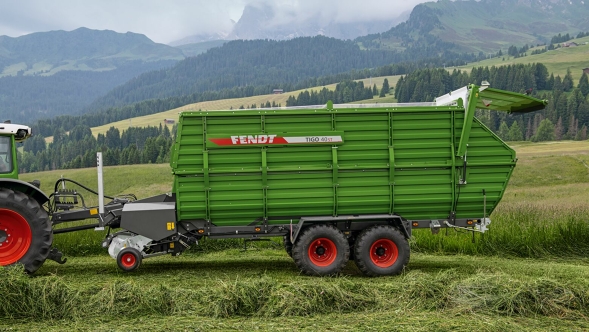 A green-painted Fendt Tigo forage wagon standing in a meadow during green forage harvesting at high altitude in the Alps