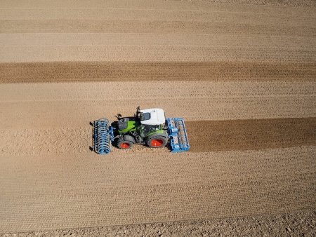 A green-painted Fendt with red rims drives on a harvested field and working the soil