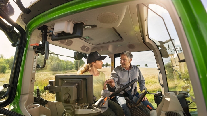 A farmer sitting on a tractor with a trainer and has FendtONE explained to her.