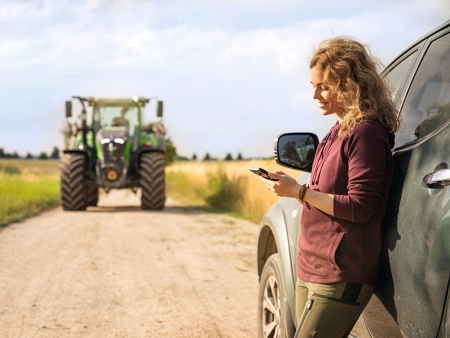 A farmer standing at the edge of the field leaning against her car and checking the documentation transfer from her Fendt 700 Vario Gen6 in FendtONE