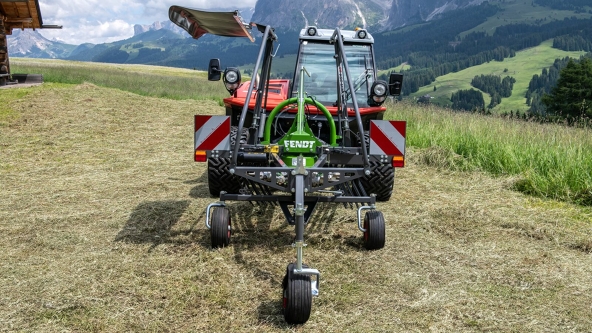 The green Fendt Alpine single-rotor rake stands on a mountain meadow with a mountain landscape in the background.