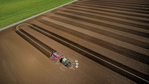 Un trattore attraversa un campo, si può vedere la precisa linea di guida del tracciato