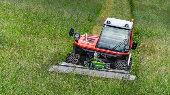 Una Fendt Slicer gamma Alpina verde falcia un prato verde e lascia la traccia di erba appena tagliata.