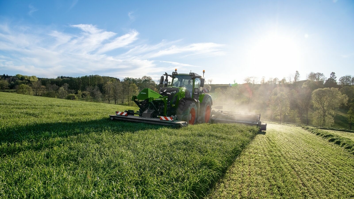 Un agricoltore guida un trattore su un prato e falcia con una falciatrice trainata Fendt