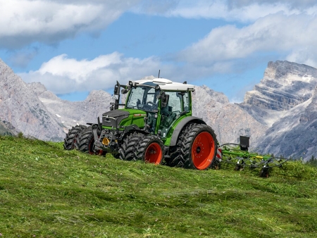 Un Fendt 200 Vario verniciato in verde con cerchioni rossi durante la raccolta di foraggio verde in ambiente alpino ad altitudini elevate