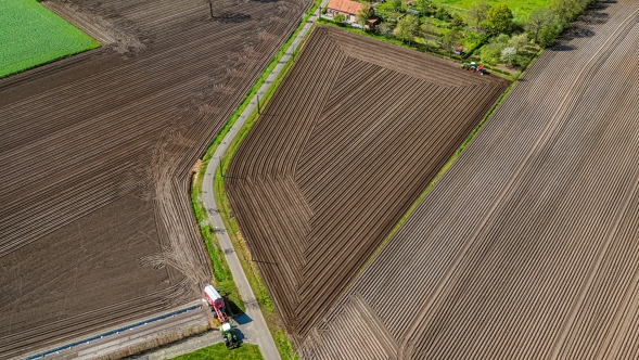 „Fendt“ traktorius važiuoja iš lauko, iš paukščio skrydžio matyti jau įdirbti laukai su vėžėmis.