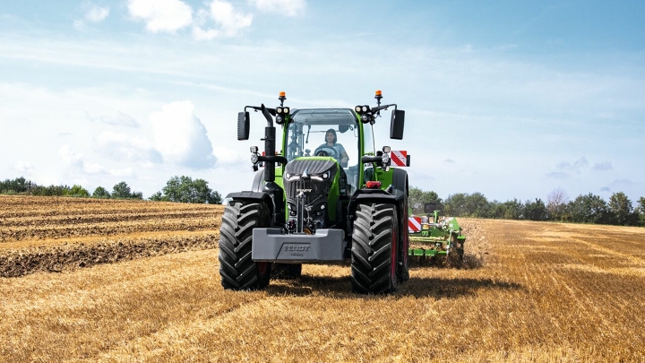 Fendt 700 Vario Gen 7 traktorius dirba lauke. Fone - medžiai ir mėlynas dangus su baltais debesimis.