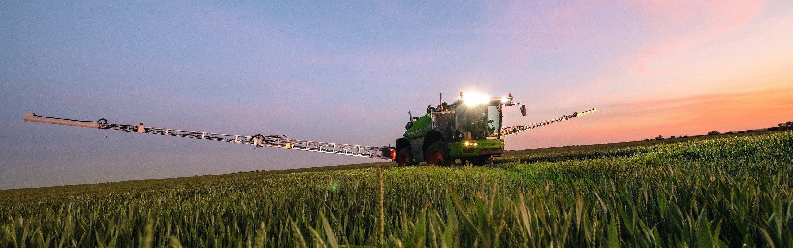 Fendt Rogator 600 Gen2 ar paceltu strēli saulrieta laikā