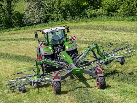 Fendt traktors brauc ar Fendt Former grābekli pa zaļo lauku.