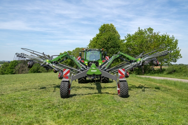 Ein Traktor steht mit einem Fendt Former Schwader auf einer Wiese.