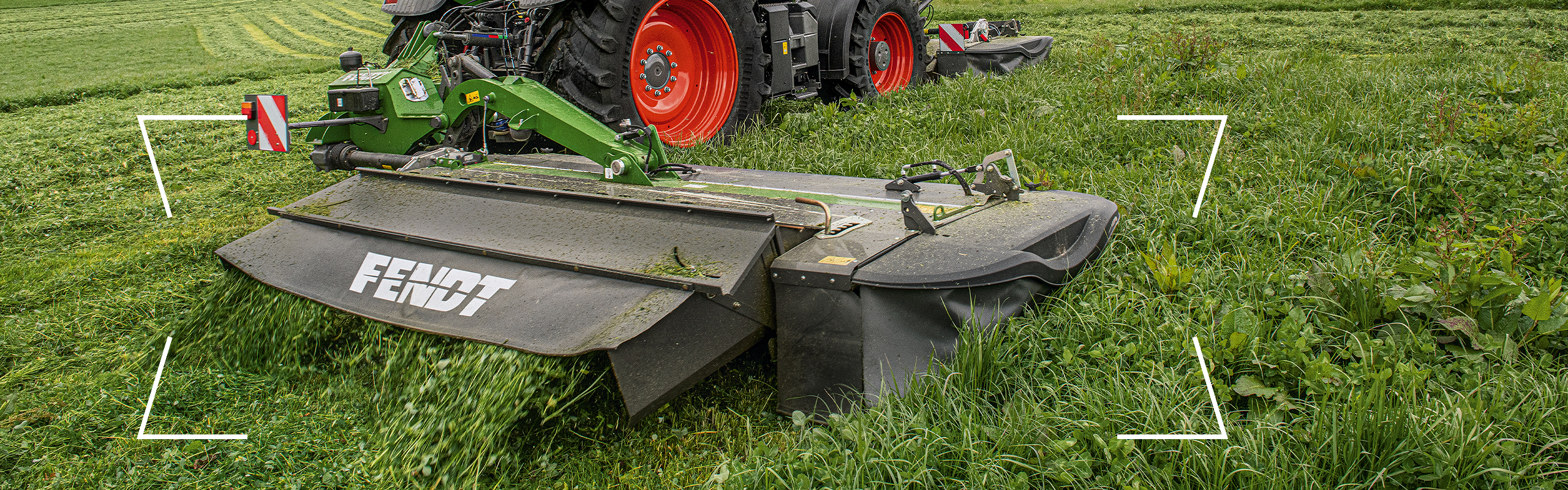 Zaļas krāsas Fendt traktors ar sarkaniem riteņu lokiem un Fendt Slicer aizmugurējo uzkari zālāju platībā lopbarības novākšanas laikā.