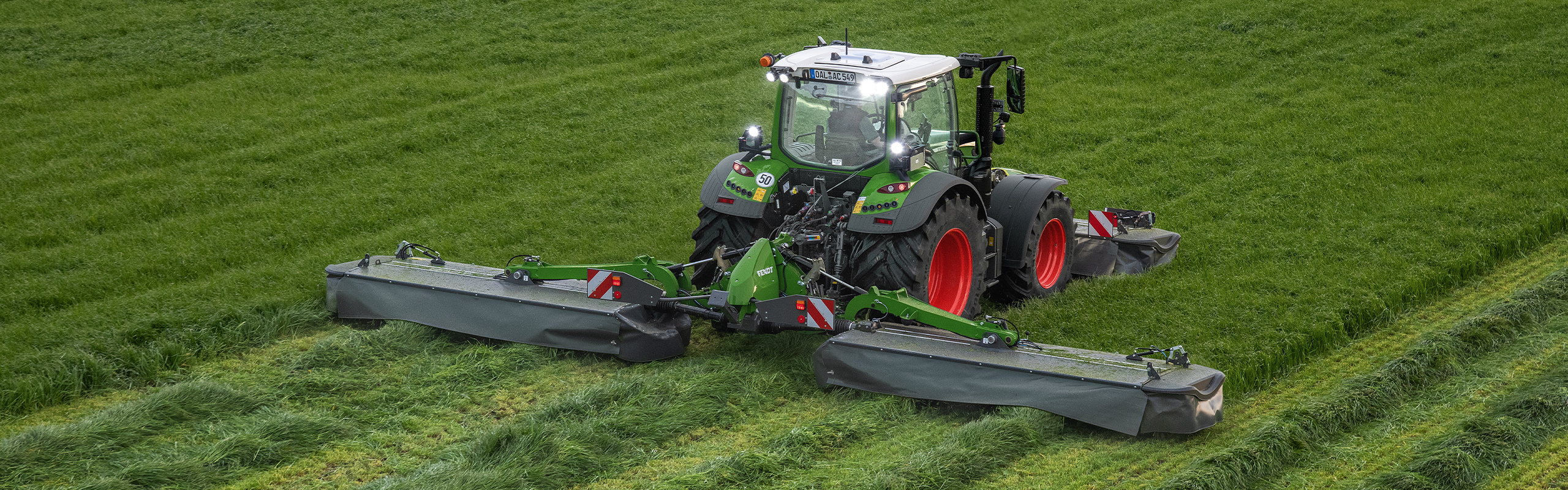 Fendt traktors ar taureņa formas aizmugurējo uzkari un priekšējo uzkari lopbarības novākšanai.