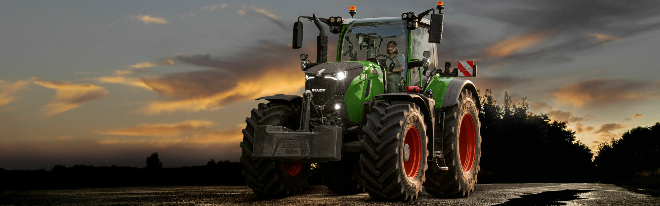 Fendt 700 Vario Gen7 traktors uz ceļa ar dramatiska saulrieta debesīm fonā