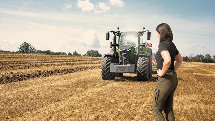 Lauksaimnieks stāv uz stiebrzāļu lauka sava Fendt 700 Vario Gen7 priekšā.