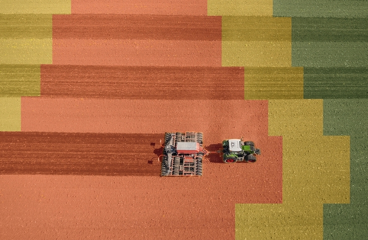 Een Fendt Vario met een zaaicombinatie rijdt over een veld dat is opgedeeld in gele, rode en groene vlakken.