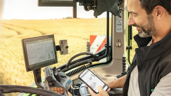 Een boer zit in de trekkercabine en heeft op zijn mobiele telefoon de Parts Books to go-app geopend.