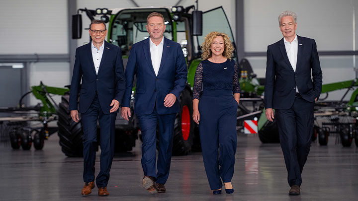 Walter Wagner, Christoph Gröblinghoff, Ingrid Bußjäger-Martin en Ekkehart Gläser staan in het Fendt Forum lachend naast elkaar voor een Fendt-trekker.