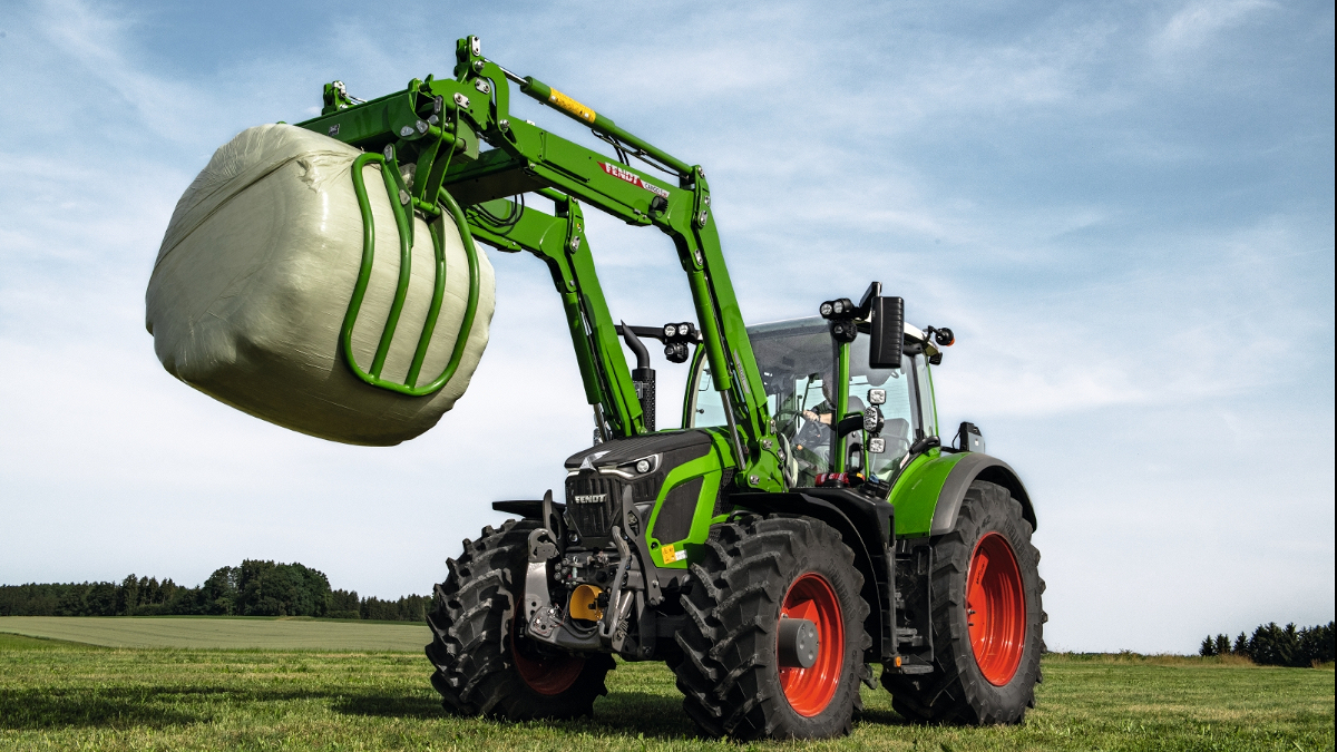 Een Fendt 600 Vario met frontlader staat in een weide en draagt een kuilbaal.