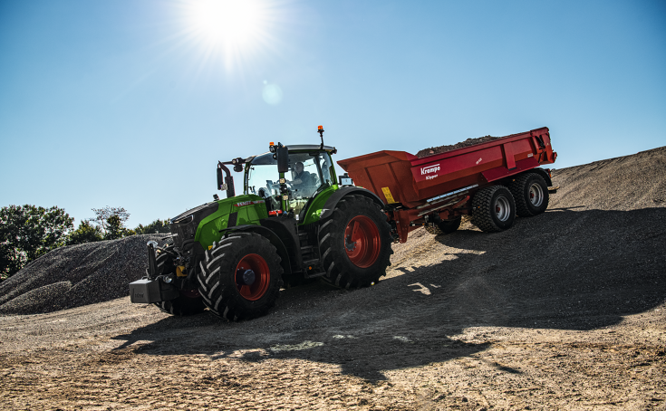 En Fendt 728 Vario med en rød Krampe tipphenger kjører ned en bakke på en byggeplass