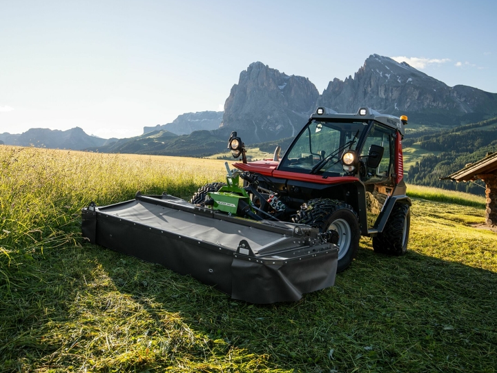 Slåmaskinen Fendt Slicer Alpine i arbeid på en eng med fjell og blå himmel i bakgrunnen