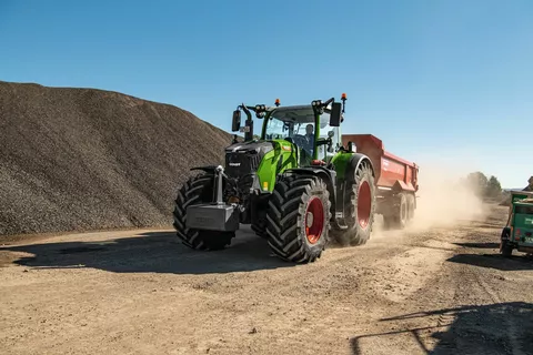 Fendt 728 Vario z czerwoną wywrotką mija górę żwiru na placu budowy.