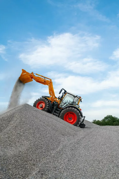 Fendt 600 Vario w komunalnym kolorze pomarańczowym wysypuje żwir z łyżki ładowacza czołowego na pryzmę.