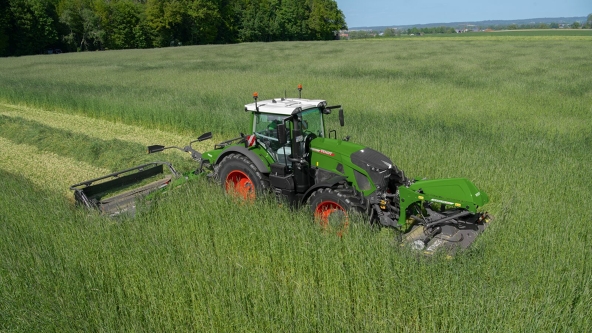 Zielony Fendt 700 Vario na łące pod błękitnym niebem z zestawem kosiarek Fendt Slicer z mocowaniem z przodu i z tyłu.