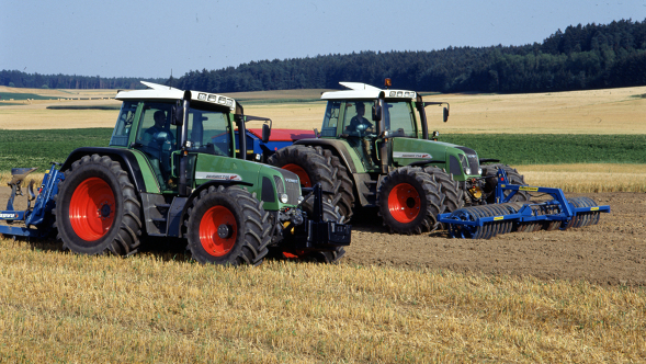 Dwa starsze ciągniki Fendt jadą obok siebie na polu.