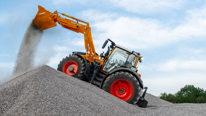 Fendt 600 Vario w komunalnym kolorze pomarańczowym wysypuje żwir z łyżki ładowacza czołowego na pryzmę.