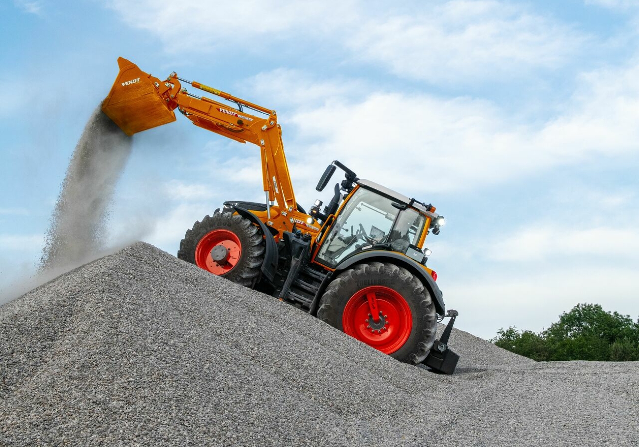 Fendt 600 Vario w komunalnym kolorze pomarańczowym wysypuje żwir z łyżki ładowacza czołowego na pryzmę.