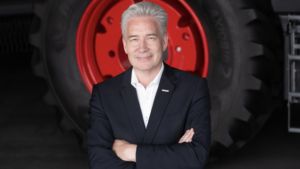 Ekkehart Gläser standing in a dark blue suit with his arms folded in front of a tractor wheel and smiling.