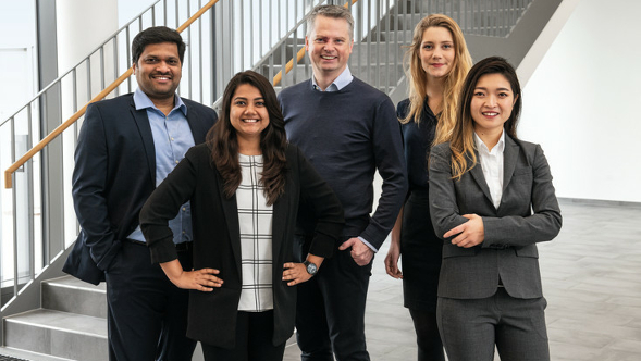 Four Fendt office employees standing next to each other in front of a staircase.