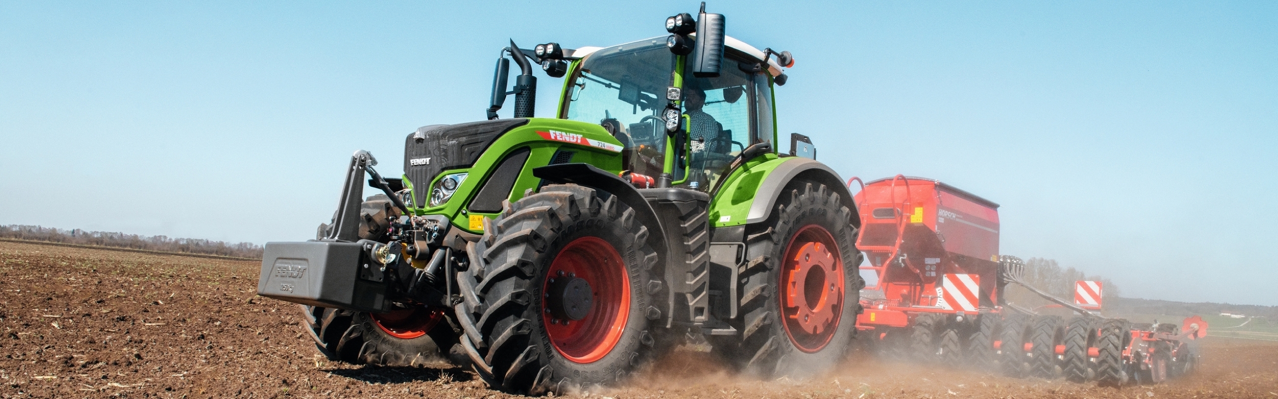 A farmer driving a Fendt 700 Vario Gen6 and a Horsch seed drill across a dusty field.