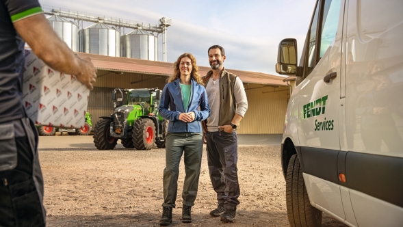 Male and female farmers standing in the driveway of their farm and greeting a Fendt service employee.
