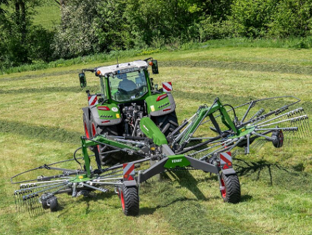 A Fendt tractor drives with a Fendt Former rake on a green field.
