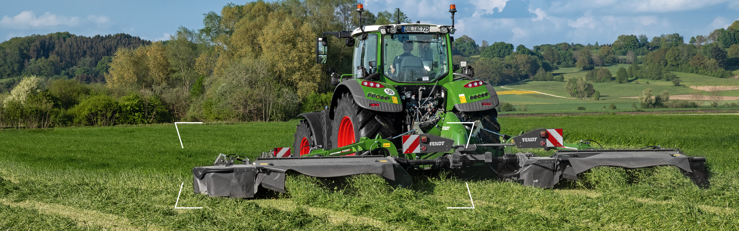 A green Fendt Vario Tractor red rims in the field equipped with mowers.