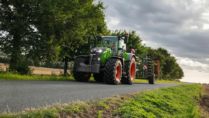 A green Fendt 700 Vario with attachment drives safely and swiftly along a country road
