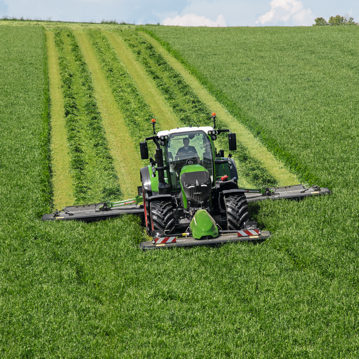 A farmer mows a green meadow with a Fendt tractor and Fendt Slicer front mower.